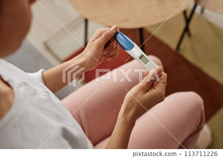 High angle closeup of female hands holding pregnancy test with blank screen sitting on sofa at home copy space High angle closeup of female hands holding pregnancy test with blank screen sitting on sofa at home copy space 113711226