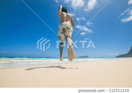 Young man in swimsuit running towards turquoise waters on a sandy Hawaiian beach Young man in swimsuit running towards turquoise waters on a sandy Hawaiian beach 113711229