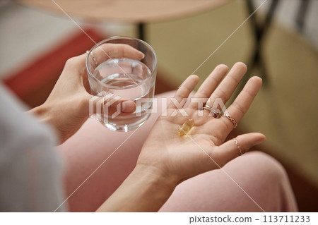 Top view closeup of unrecognizable woman taking vitamins at home and holding jelly pill in open hand copy space Top view closeup of unrecognizable woman taking vitamins at home and holding jelly pill in open hand copy space 113711233