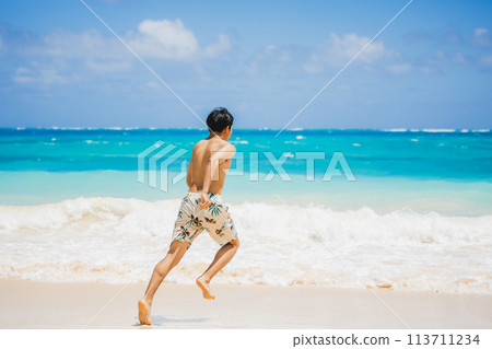 Young man in swimsuit running towards turquoise waters on a sandy Hawaiian beach 113711234