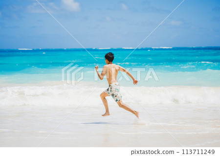 穿著泳衣的年輕人跑向夏威夷沙灘上的碧綠海洋 113711249