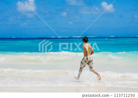 Young man in swimsuit running towards turquoise waters on a sandy Hawaiian beach Young man in swimsuit running towards turquoise waters on a sandy Hawaiian beach 113711250
