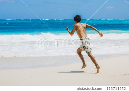 Young man in swimsuit running towards turquoise waters on a sandy Hawaiian beach 113711252
