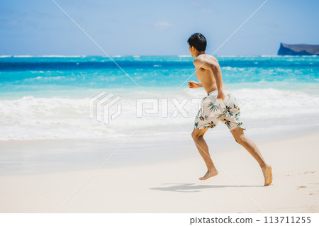 Young man in swimsuit running towards turquoise waters on a sandy Hawaiian beach Young man in swimsuit running towards turquoise waters on a sandy Hawaiian beach 113711255