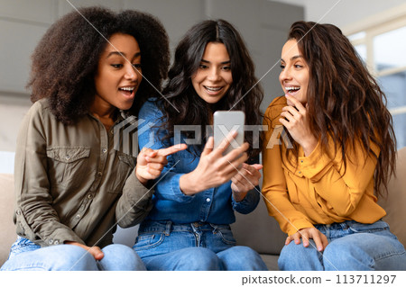 Captivated friends viewing a smartphone at home Captivated friends viewing a smartphone at home 113711297