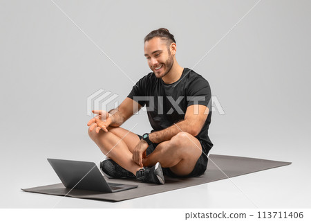 Man with laptop laughing on fitness mat 113711406