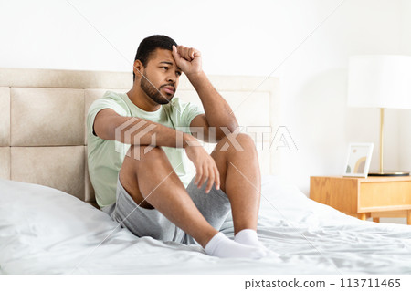 Man sitting on bed looking thoughtful Man sitting on bed looking thoughtful 113711465