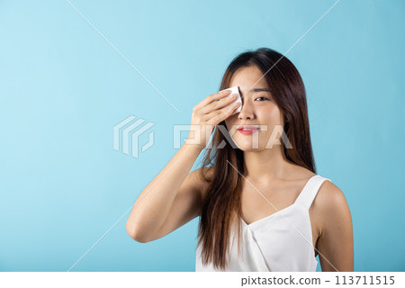 Facial Beauty Treatment Hygiene skin. Asian beautiful young woman removing cosmetic make up using pad cotton face cleaner disc, studio shot isolated on blue background, Happy female cleaning eyes Facial Beauty Treatment Hygiene skin. Asian beautiful young woman removing cosmetic make up using pad cotton face cleaner disc, studio shot isolated on blue background, Happy female cleaning eyes 113711515