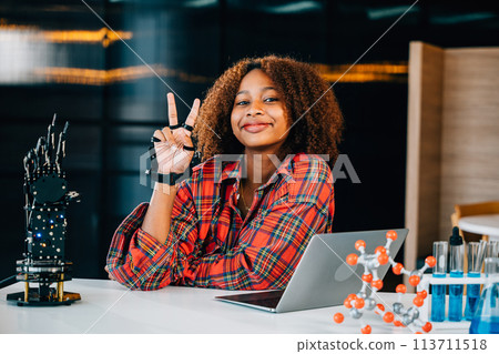 In a classroom setting a Black teenage student explores a robotic arm engaging in learning subjects of interest. Embracing innovation and technology for skill development and joy in education. 113711518