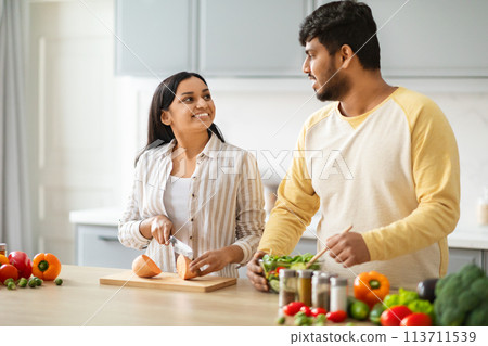 Indian Spouses Having Conversation While Preparing Food In Cozy Kitchen 113711539