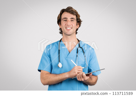 Smiling male nurse in scrubs writing on clipboard Smiling male nurse in scrubs writing on clipboard 113711589