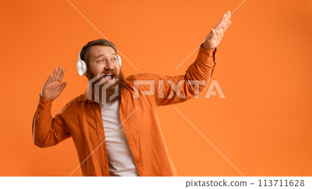 Positive Bearded Guy In Wireless Headset Dancing Over Orange Wall Positive Bearded Guy In Wireless Headset Dancing Over Orange Wall 113711628