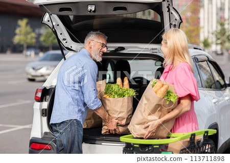 Retired couple storing groceries in car trunk 113711898