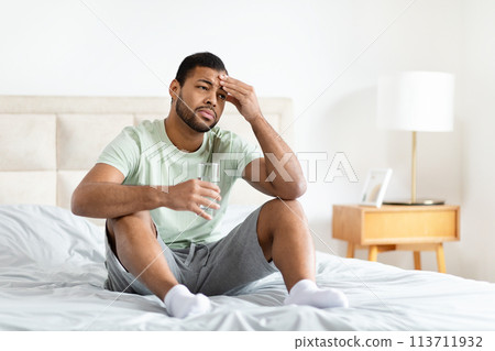 Man sitting on bed with glass of water Man sitting on bed with glass of water 113711932