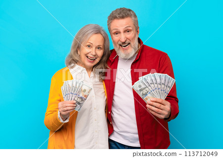 senior man and woman holding money cash against blue backdrop senior man and woman holding money cash against blue backdrop 113712049