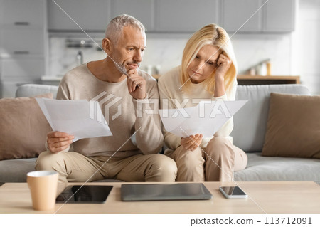Concerned couple reviewing papers with serious faces Concerned couple reviewing papers with serious faces 113712091