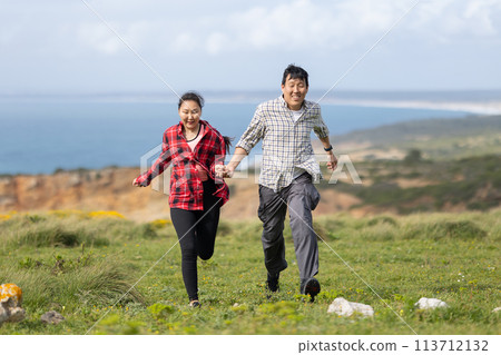 A couple running on a grassy hill overlooking the ocean 113712132