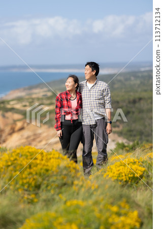 A couple standing on a hillside with a beautiful view of the ocean 113712134