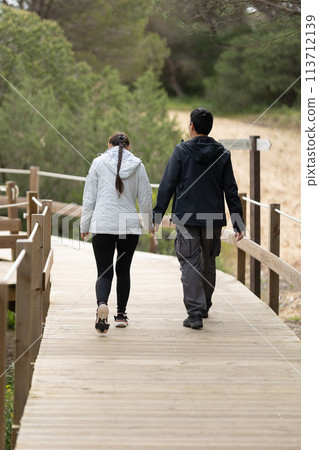 A man and woman are walking on a wooden bridge - rear view A man and woman are walking on a wooden bridge - rear view 113712139