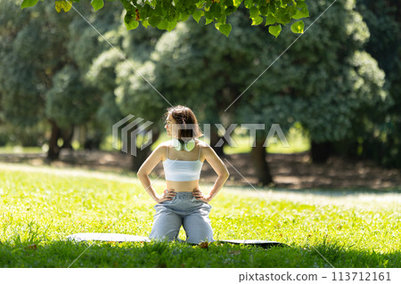 A woman is sitting on the grass in a park A woman is sitting on the grass in a park 113712161