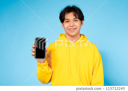 Smiling teen showing smartphone on blue background Smiling teen showing smartphone on blue background 113712245