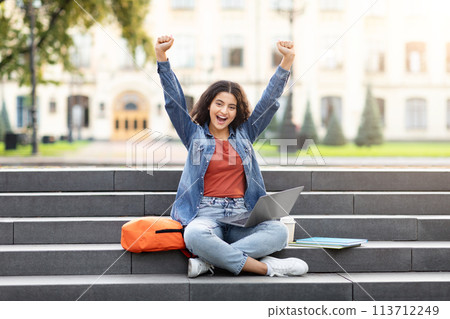 Excited student with laptop on campus steps Excited student with laptop on campus steps 113712249