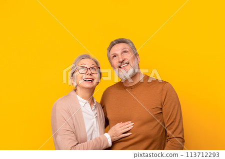 Cheerful senior couple posing together hugging looking up, yellow background 113712293