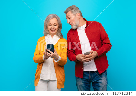 Jealous Senior Husband Peeking At Wife's Smartphone On Blue Background 113712314