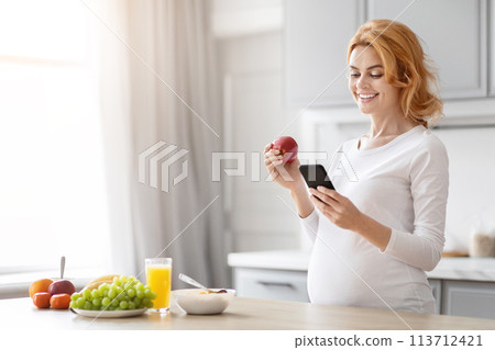 Pregnant woman checking phone with fruit in her hand Pregnant woman checking phone with fruit in her hand 113712421