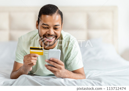 Man holding card and phone in bed Man holding card and phone in bed 113712474