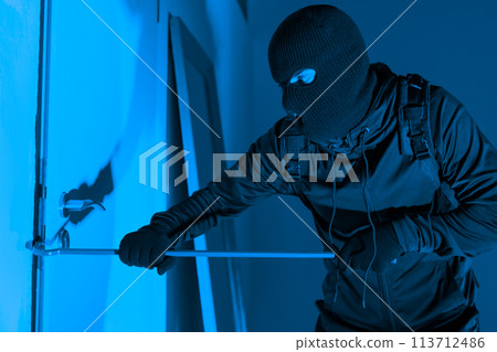 Masked burglar prying window open with crowbar 113712486
