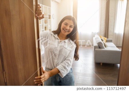 Welcoming indian woman at home opening door with smile Welcoming indian woman at home opening door with smile 113712497