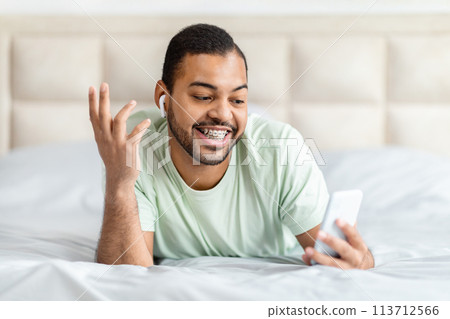 Man with earbud gesturing in bed 113712566