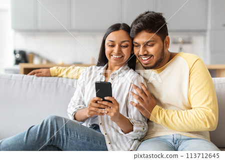 Indian Man and Woman Sitting on Couch Looking at Cell Phone Indian Man and Woman Sitting on Couch Looking at Cell Phone 113712645