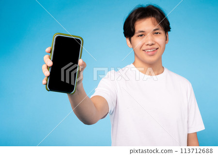 Happy guy showing smartphone screen, blue background Happy guy showing smartphone screen, blue background 113712688