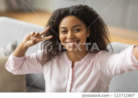 Lady taking selfie with peace sign at home 113712867
