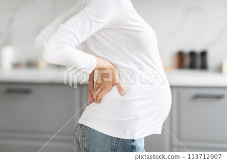 Pregnant woman touches her back gently, cropped 113712907