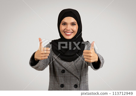Joyful hijab-wearing woman giving thumbs up in suit 113712949