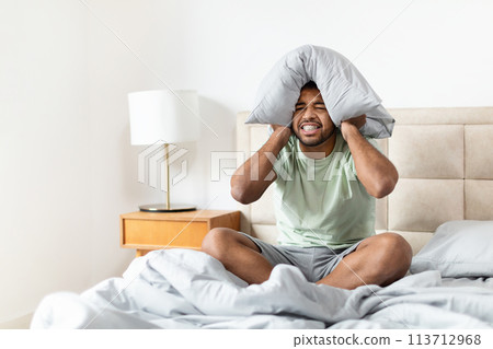 Man annoyed by noise covering ears with pillow Man annoyed by noise covering ears with pillow 113712968