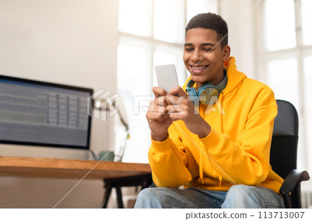 Happy teen guy using smartphone with headphones on Happy teen guy using smartphone with headphones on 113713007