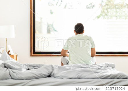Man sitting on bed facing window 113713024