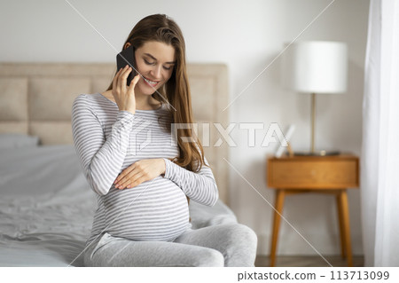 Pregnant woman talking on phone in bedroom Pregnant woman talking on phone in bedroom 113713099