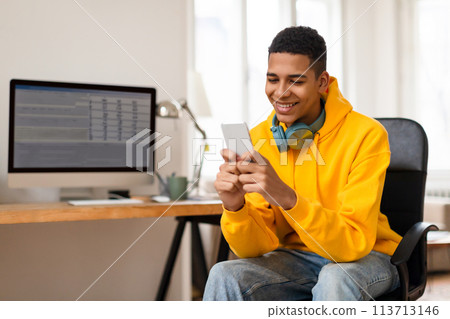 Smiling young man using smartphone at desk 113713146