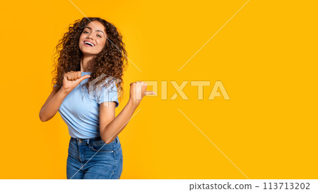 Joyful woman pointing aside with thumb on yellow Joyful woman pointing aside with thumb on yellow 113713202