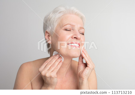 Elderly lady cleaning face with cotton pad 113713210