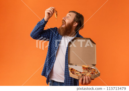 Redhaired bearded man in casual attire eats juicy pizza, studio Redhaired bearded man in casual attire eats juicy pizza, studio 113713479