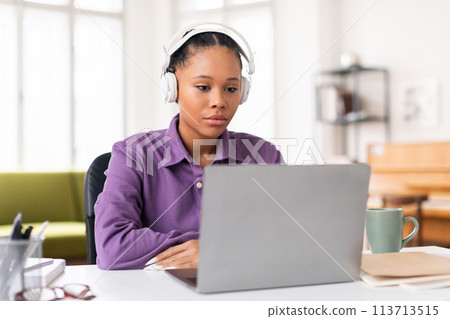 Focused female student with headphones looking at laptop screen 113713515