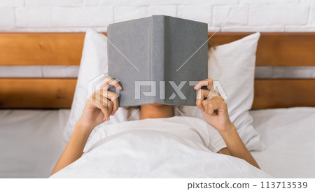 Woman reading book and covering face, lying in bed 113713539