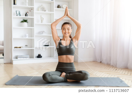 Peaceful young asian woman in activewear practicing yoga at home 113713607