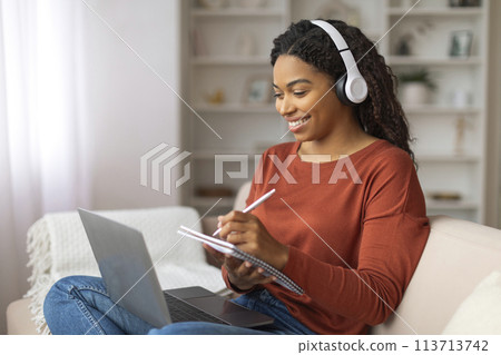 Black Woman Sitting on Couch With Laptop and Headphones Black Woman Sitting on Couch With Laptop and Headphones 113713742
